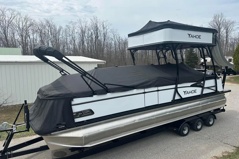 Slide: The Image of 2025 Tahoe 2785 pontoon boat with black cover on trailer, parked outdoors. - 2