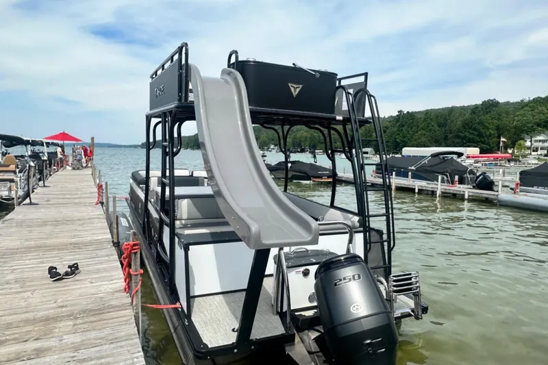 Slide: The Image of 2025 Tahoe 2785 pontoon boat with slide docked at a lakeside marina. - 3
