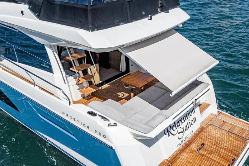 Slide: The Image of 2019 Prestige 520 yacht with outdoor seating, awning, and "Relaxation Station" name, on the water. - 5