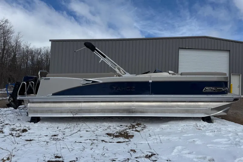 Slide: The Image of 2025 Tahoe 2585 pontoon boat parked on snowy ground near a metal building. - 1