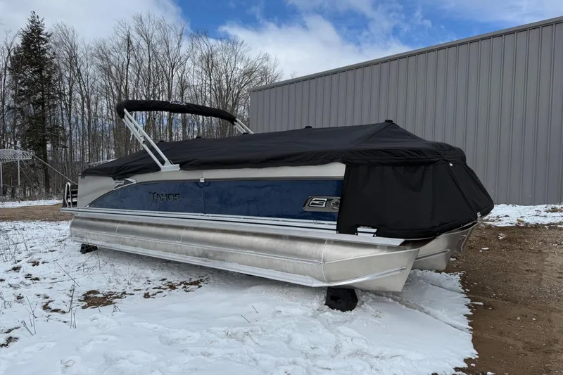 Slide: The Image of 2025 Tahoe 2585 pontoon boat covered in snow, parked beside a metal building. - 4