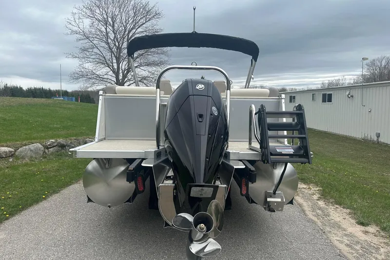 Slide: The Image of 2025 Tahoe 2585 pontoon boat with outboard motor, parked on a paved path. - 3