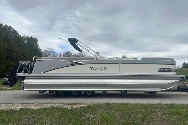 Slide: The Image of 2025 Tahoe 2585 pontoon boat on trailer, parked outdoors under cloudy sky. - 7