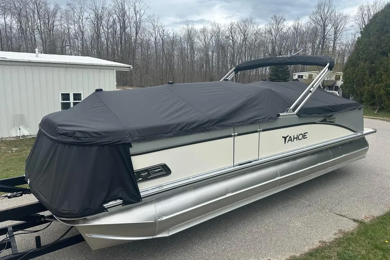 Slide: The Image of 2025 Tahoe 2585 pontoon boat with black cover, parked on a driveway near trees. - 8