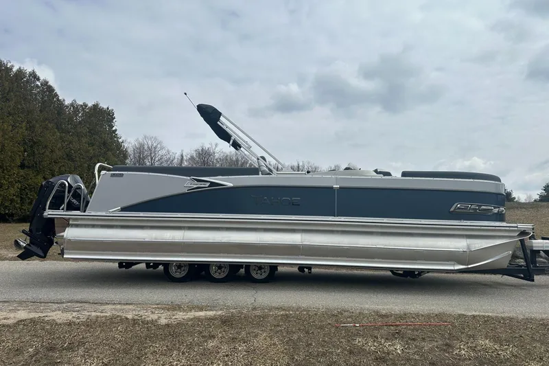 Slide: The Image of 2025 Tahoe 2585 pontoon boat on trailer, parked on roadside under cloudy sky. - 6