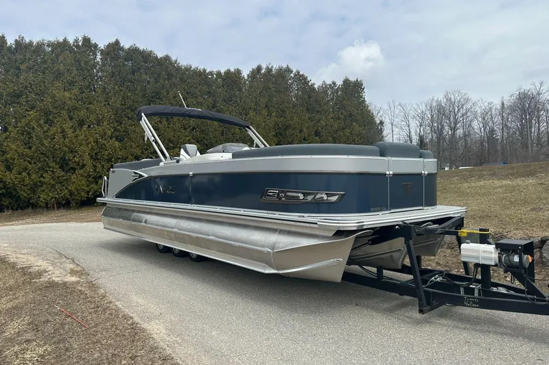 Slide: The Image of 2025 Tahoe 2585 pontoon boat on trailer, parked on a road with trees in background. - 7