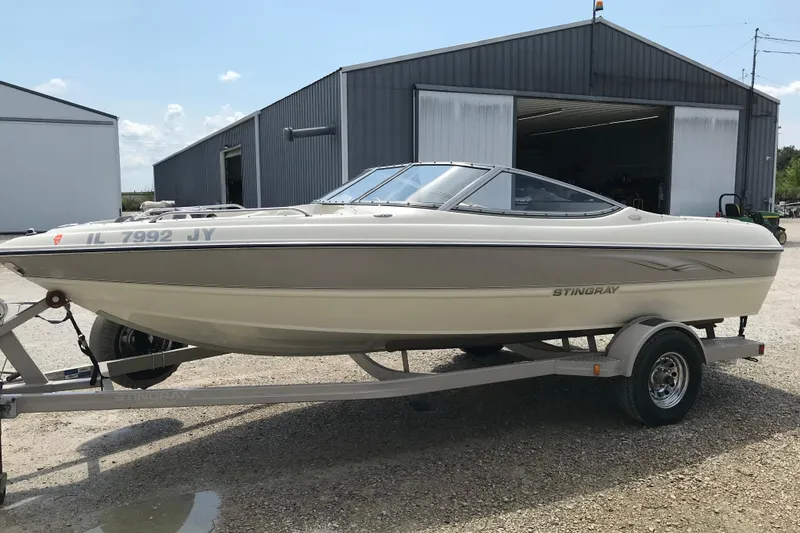 Slide: The Image of 2005 Stingray 195 LR boat on trailer, parked outside a large metal building. - 2