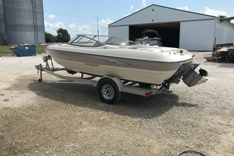 Slide: The Image of 2005 Stingray 195 LR boat on trailer, parked outdoors near a large building. - 5