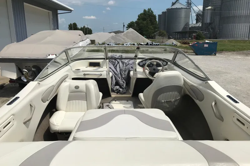 Slide: The Image of 2005 Stingray 195 LR boat interior with white seating and dashboard, parked outdoors. - 8