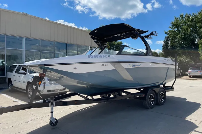 The Image of 2014 Tigé 23 boat on trailer, parked outside dealership under blue sky. - 0