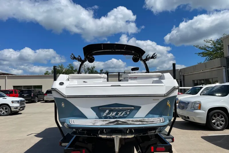 Slide: The Image of 2014 Tigé 23 boat on trailer, parked outdoors under a blue sky. - 2