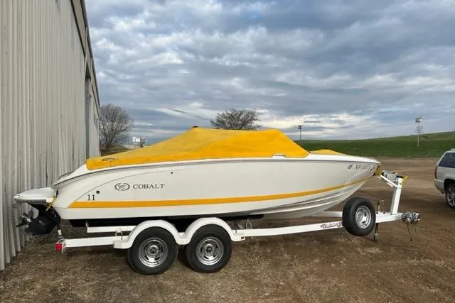The Image of 2011 Cobalt 200 boat with yellow cover on trailer, parked outdoors. - 0