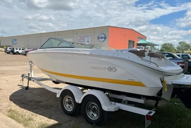 Slide: The Image of 2011 Cobalt 200 boat on trailer, parked outdoors near a warehouse. - 2