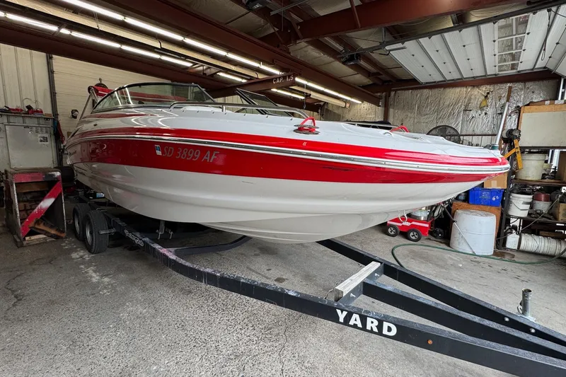 The Image of 2011 Crownline 252 EX boat in a garage, red and white design, on a trailer. - 1