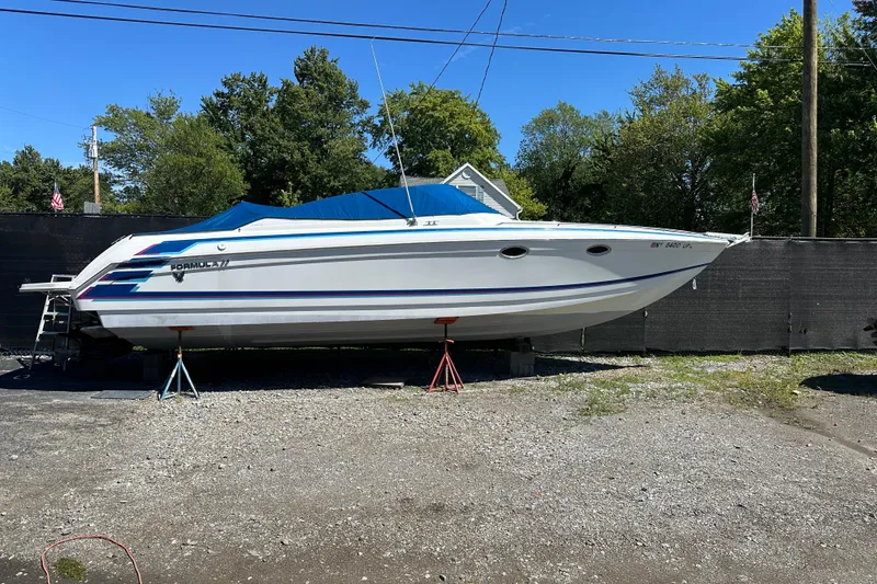 The Image of 1997 Formula 330 SS boat on stands, covered, outdoors, with trees and clear sky background. - 0