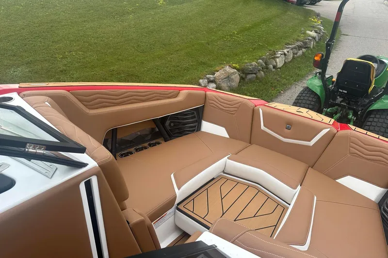 Slide: The Image of 2025 Nautique G23 boat interior with tan and white seating, parked near green grass. - 35