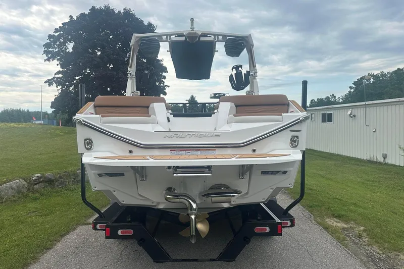 Slide: The Image of 2025 Nautique G23 boat rear view, parked on a driveway with lush greenery. - 4