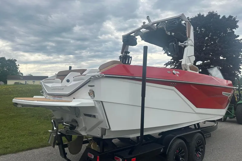 Slide: The Image of 2025 Nautique G23 boat with red and white design on a trailer under cloudy sky. - 8