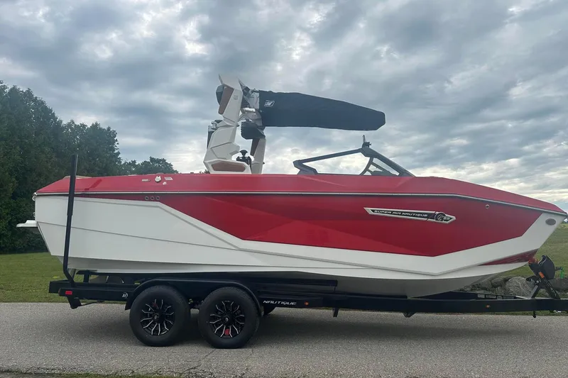 Slide: The Image of 2025 Nautique G23 boat in red and white on a trailer, under cloudy sky. - 9