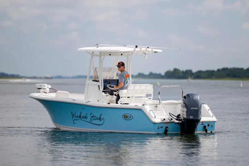Slide: The Image of 2016 Sea Hunt Ultra 225 boat on water, person steering, blue and white design. - 2