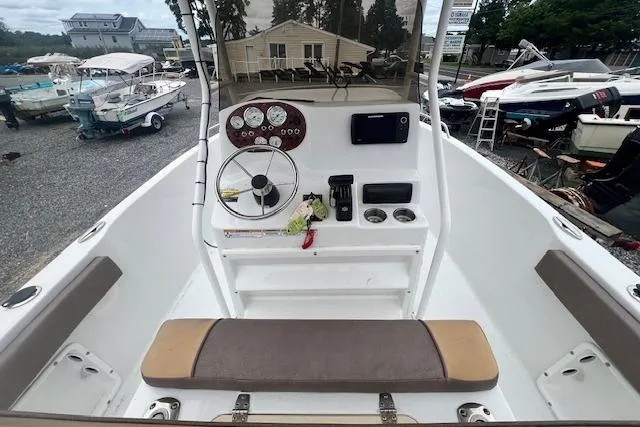 Slide: The Image of 2019 Key Largo 2100 WI boat cockpit with steering wheel, gauges, and seating in a marina setting. - 2