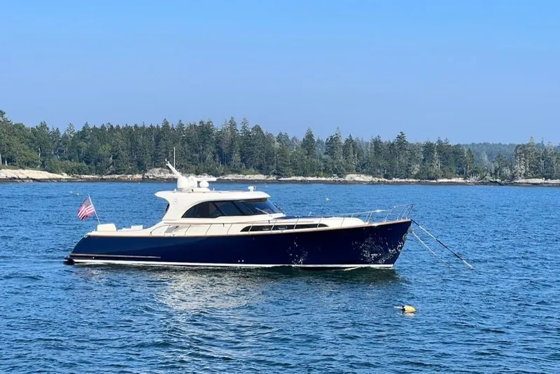 The Image of 2006 Mochi Craft 51 Dolphin yacht anchored on serene blue waters with forested shoreline. - 0