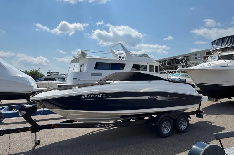 Slide: The Image of 2014 Sea Ray 220 Sundeck Outboard on trailer, parked at marina under blue sky. - 0