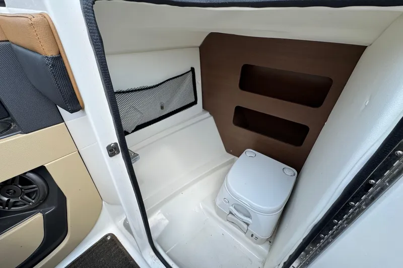 Slide: The Image of 2014 Sea Ray 220 Sundeck Outboard interior with compact marine toilet and storage shelves. - 15