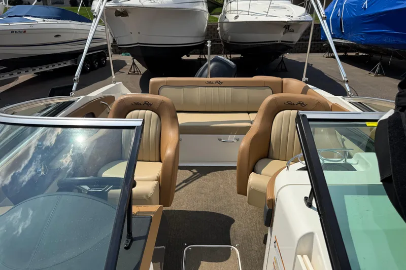 Slide: The Image of 2014 Sea Ray 220 Sundeck Outboard interior with tan seating and windshield, docked among boats. - 19