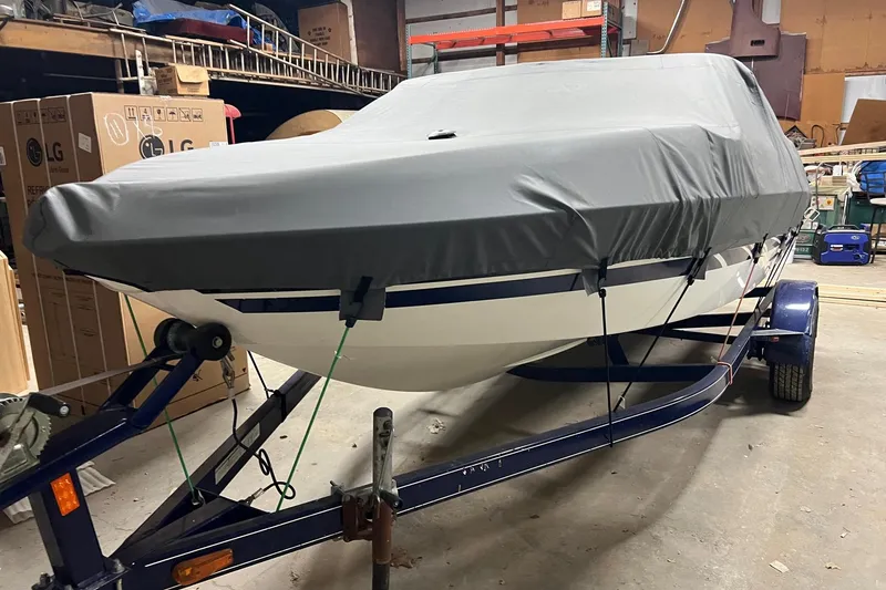 The Image of 2007 Glastron MX 175 boat covered and secured on a trailer in a storage area. - 1