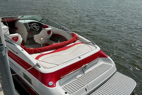 Slide: The Image of 2006 Crownline 266 boat with red and white interior, docked on calm water. - 2
