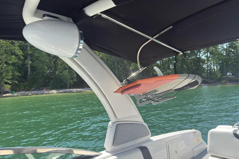 Slide: The Image of 2024 Chaparral 26 Surf boat with wakeboard rack on a sunny lake. - 19