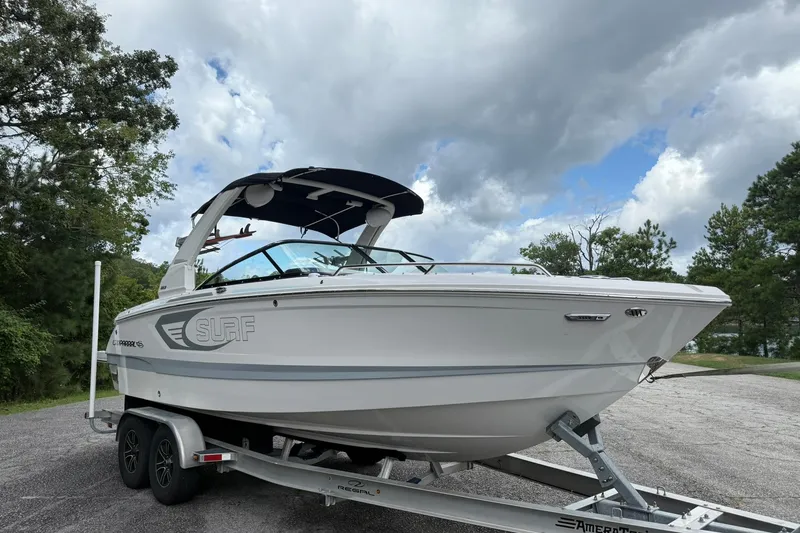 Slide: The Image of 2024 Chaparral 26 Surf boat on trailer, parked outdoors under cloudy sky. - 2