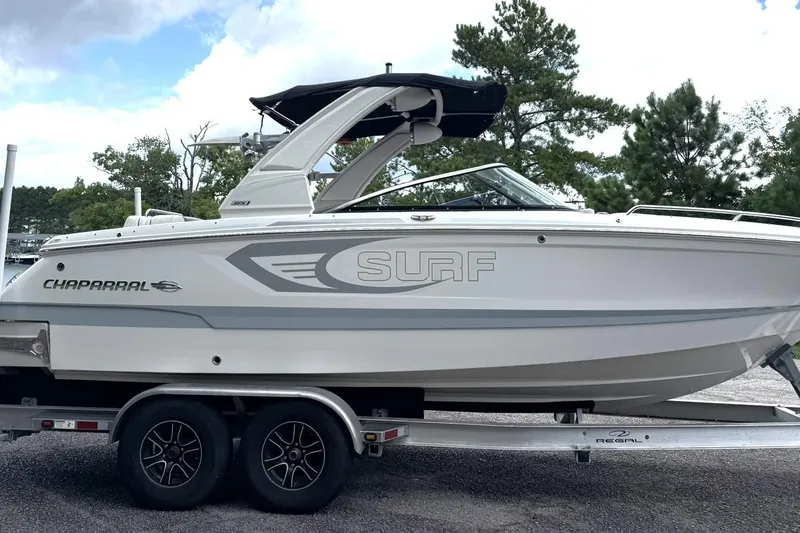 Slide: The Image of 2024 Chaparral 26 Surf boat on trailer, white exterior, parked outdoors. - 3