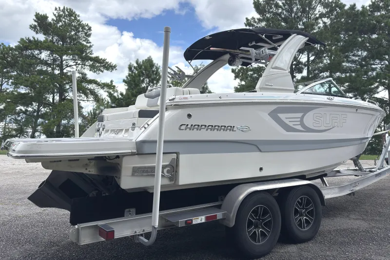 Slide: The Image of 2024 Chaparral 26 Surf boat on trailer, parked outdoors with trees in background. - 4