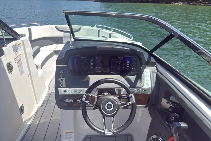 Slide: The Image of 2024 Chaparral 26 Surf boat dashboard with steering wheel and digital displays on a lake. - 8
