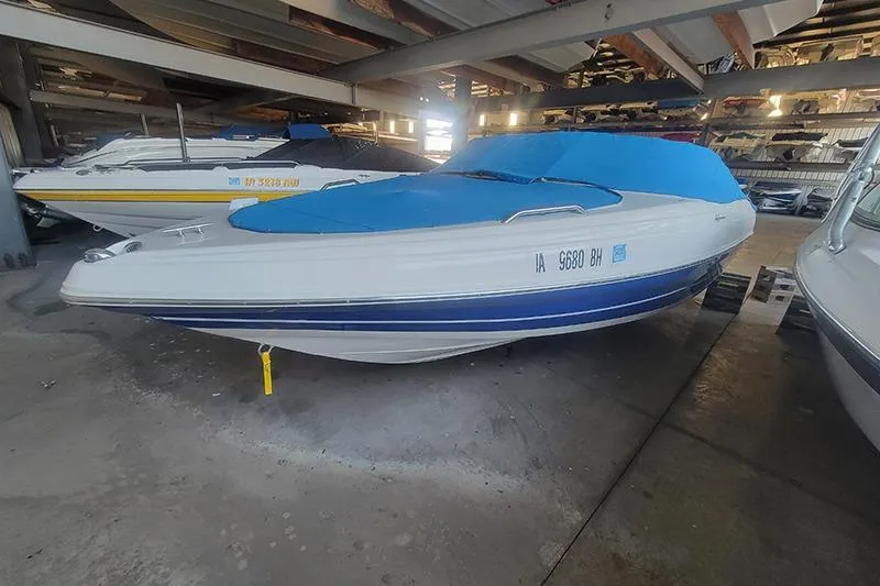 The Image of 2005 Rinker 212 boat with blue cover stored indoors. - 1