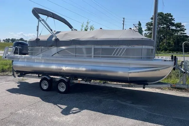 The Image of 2025 Bennington L22 pontoon boat on trailer, covered and parked outdoors. - 0