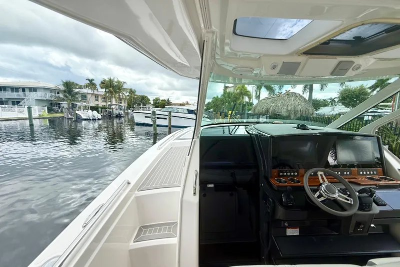 Slide: The Image of 2019 Tiara Sport 38 LS boat interior with helm, docked near waterfront homes. - 11