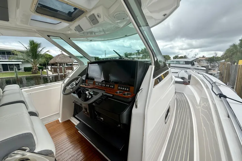 Slide: The Image of 2019 Tiara Sport 38 LS boat interior with modern helm and seating, docked by palm trees. - 8