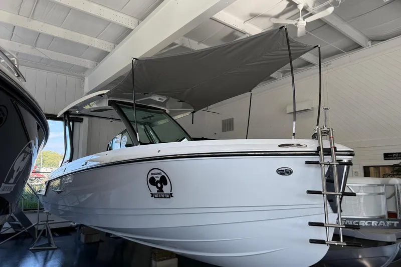 Slide: The Image of 2026 Monterey Elite 25 OB boat displayed indoors with canopy and ladder. - 0