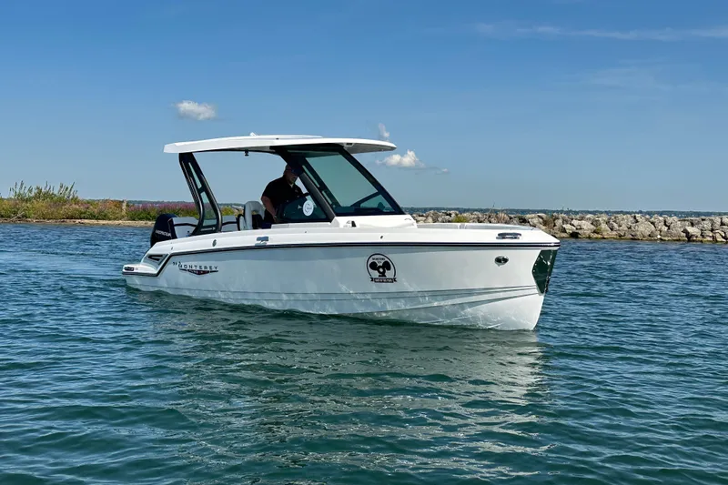 Slide: The Image of 2026 Monterey Elite 25 OB boat on water, clear sky, rocky shoreline in background. - 3