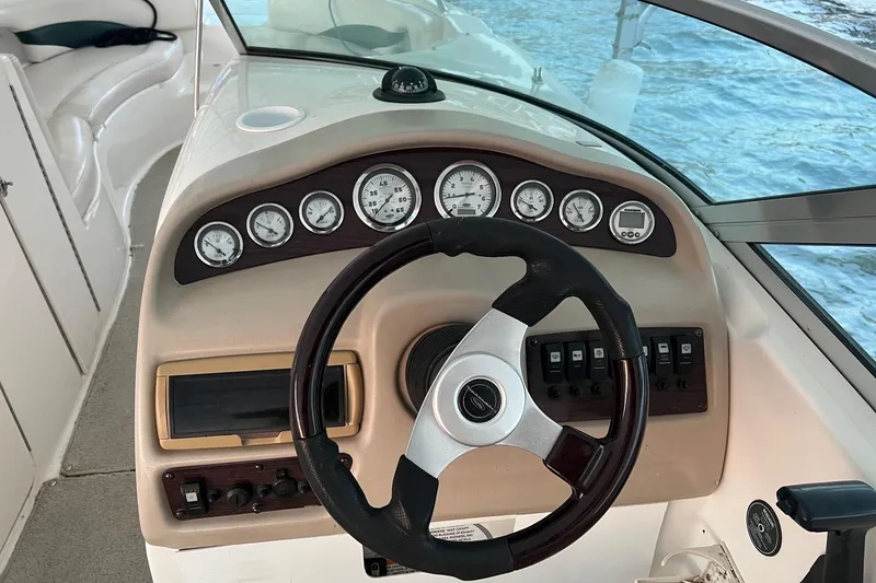 Slide: The Image of 2001 Chaparral Sunesta 233 boat dashboard with steering wheel and gauges, overlooking water. - 2