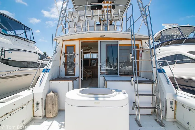 Slide: The Image of 1986 Bertram 42 Convertible yacht docked, showcasing rear deck and ladder under clear blue sky. - 5