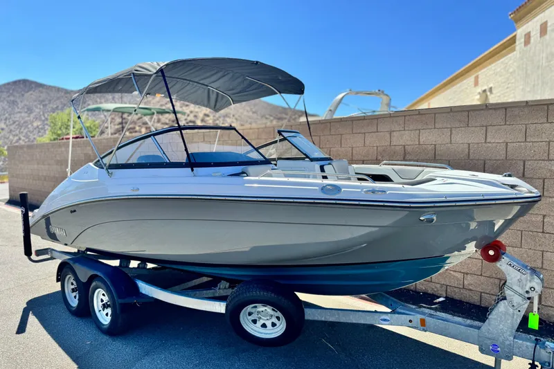 Slide: The Image of 2022 Yamaha Boats 212 on trailer, featuring sleek design and canopy, parked outdoors. - 1
