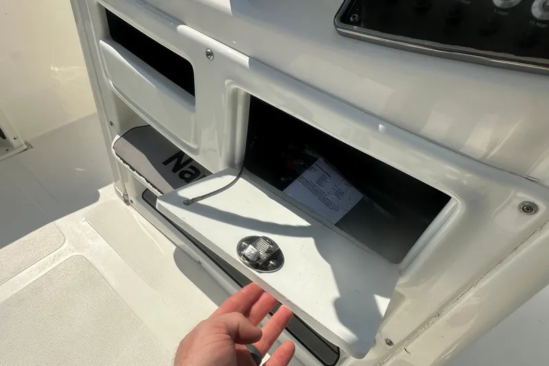 Slide: The Image of 2023 NauticStar 2102 Legacy boat storage compartment with open hatch and visible hand. - 23