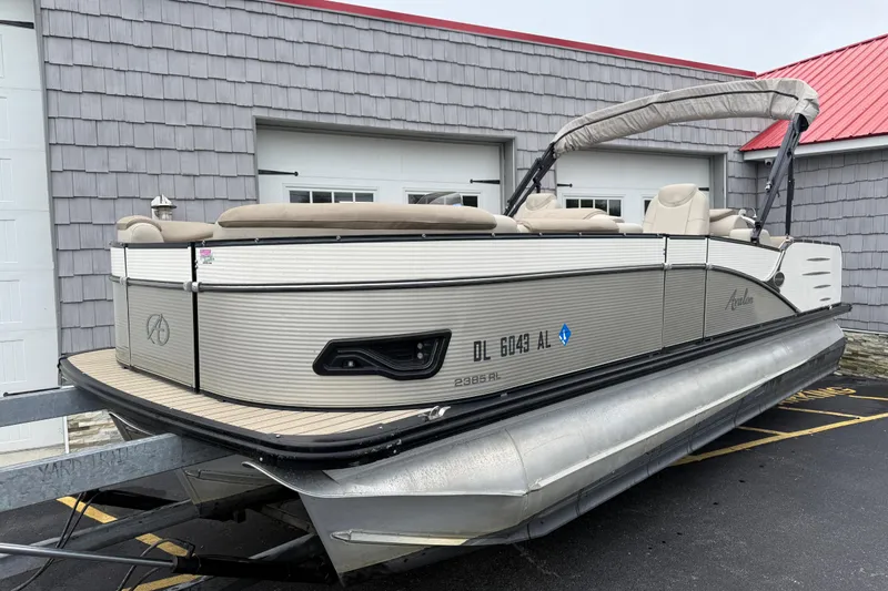 Slide: The Image of 2018 Avalon 2385 Catalina Rear Lounger Tri-Toon boat on trailer, parked by building. - 2