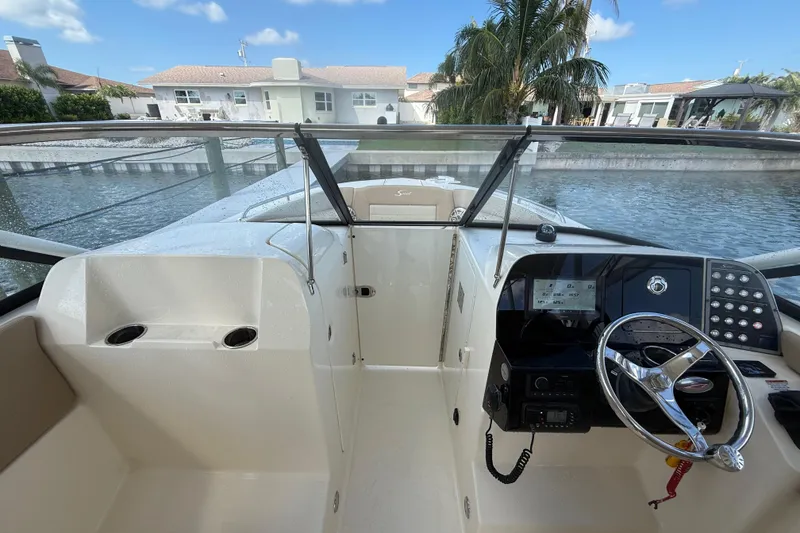 Slide: The Image of 2023 Scout 255 Dorado boat interior with steering wheel and dashboard, docked by waterfront homes. - 35