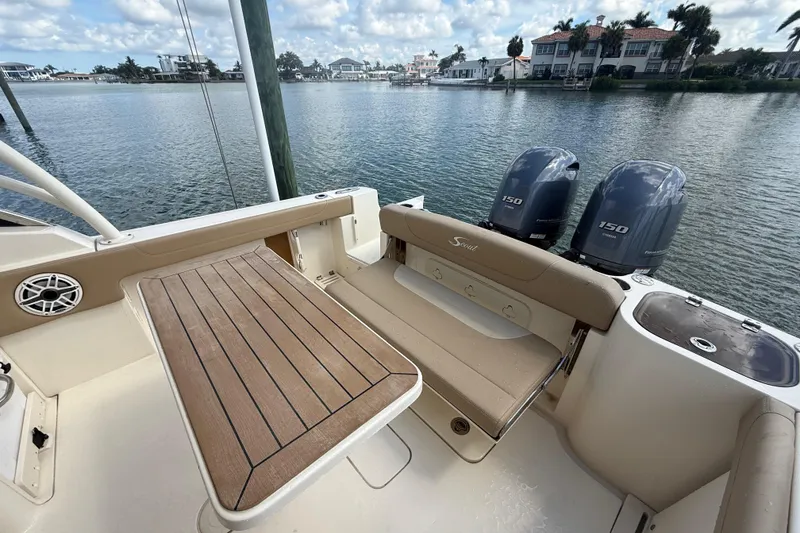 Slide: The Image of 2023 Scout 255 Dorado boat interior with twin engines, wooden table, and waterfront view. - 78