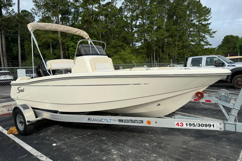 Slide: The Image of 2026 Scout 188 Sportfish boat on trailer, parked in a lot with trees in background. - 3